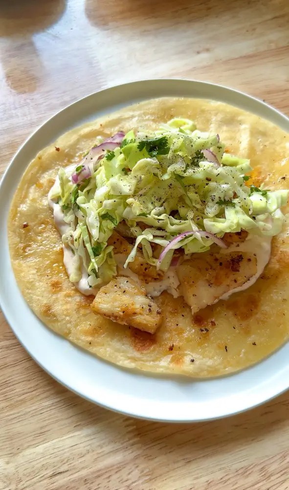 flour tortilla on a plate with fish and cabbage