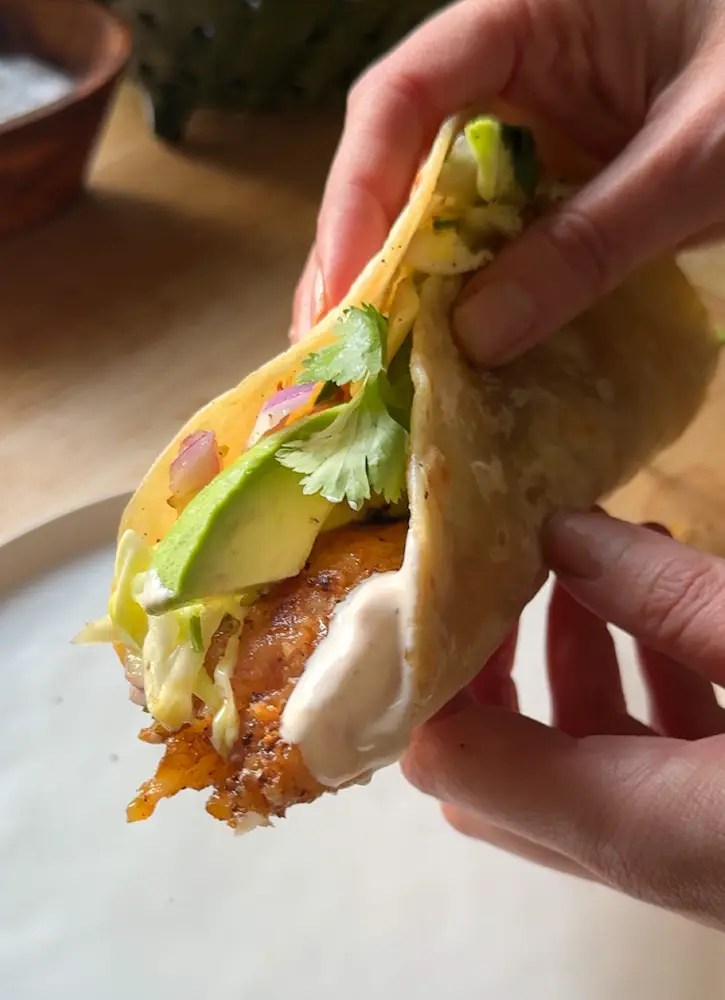 hand holding flour tortilla with fish and avocado
