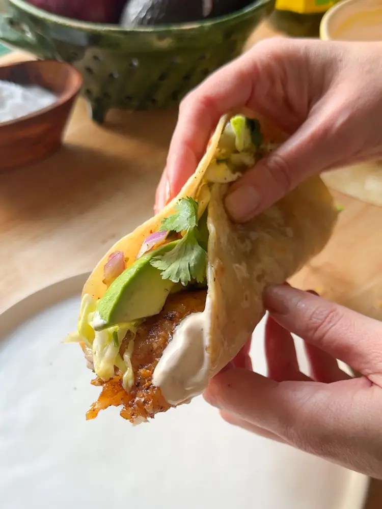 hand holding fish taco over plate