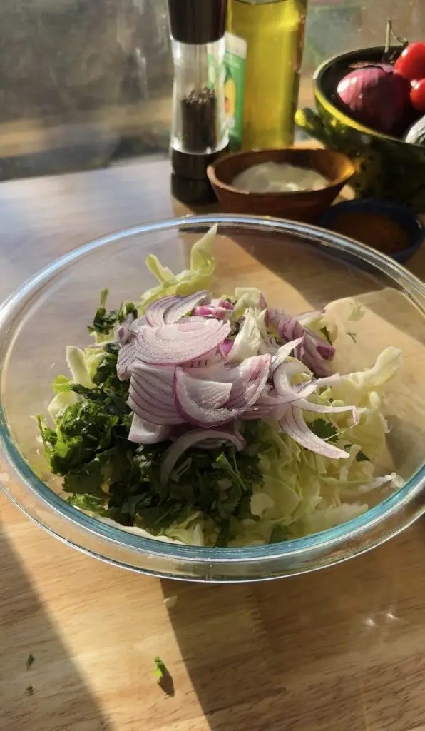 glass bowl with cabbage, cilantro, and sliced red onion