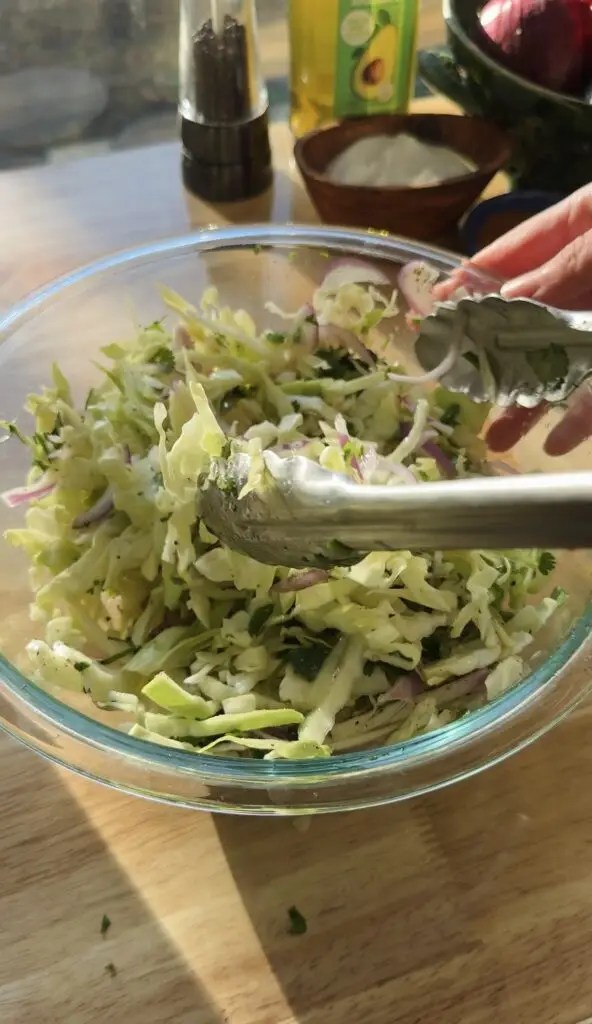 cabbage slaw in glass bowl with tongs in it