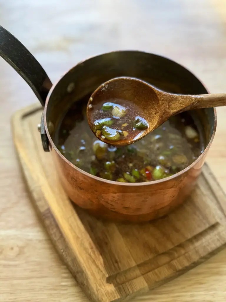Soy garlic wing sauce in a saucepan with a spoon scooping some up.