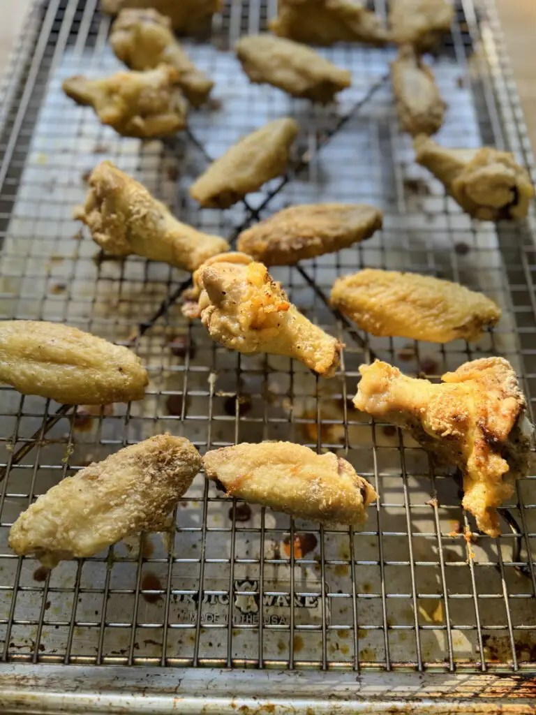 Cooked wings on a sheet pan lined with a wire rack before coating in sauce.
