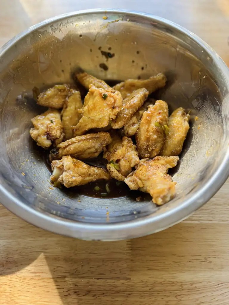 Cooked chicken wings in a mixing bowl with the sauce.