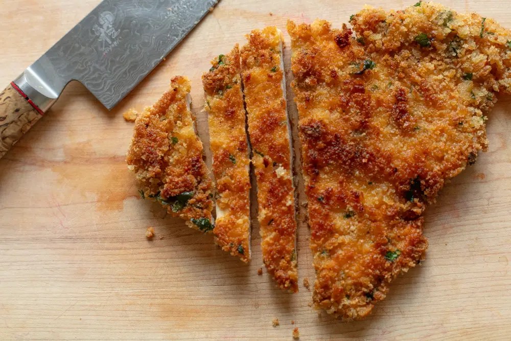 Close up of chicken schnitzel on a cutting board with some slices off the end.