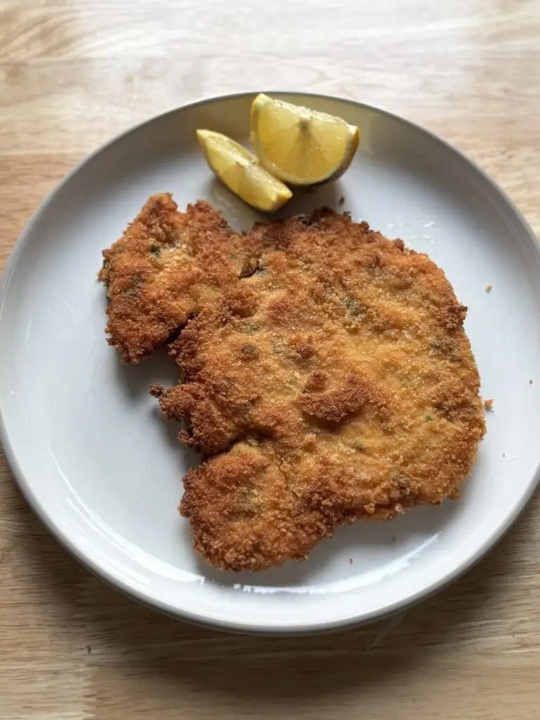Chicken schnitzel served on a plate with lemon wedges on the side.