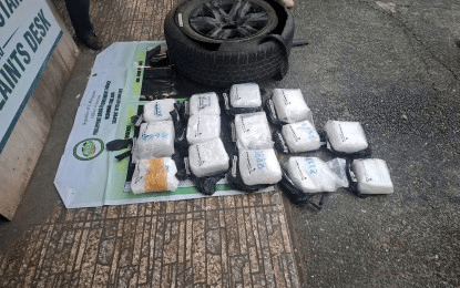 A tire is propped against a surface with several wrapped packages arranged on the ground, indicating a possible contraband situation.