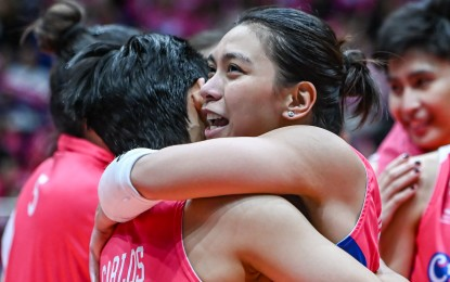 Two volleyball players embrace each other in celebration after a game, wearing matching pink jerseys.