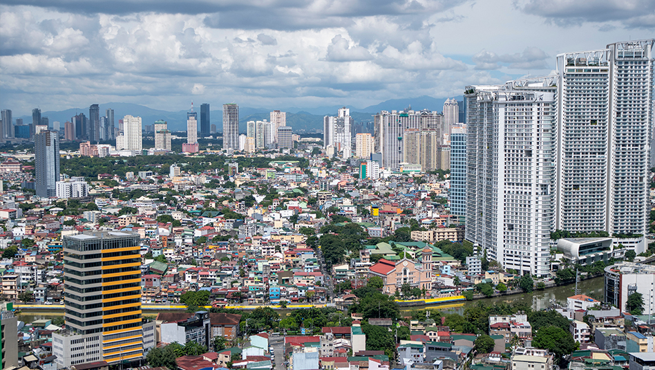 A panoramic view of a city skyline featuring a mix of modern skyscrapers and traditional buildings, with greenery and a river flowing through the urban landscape under a partly cloudy sky.