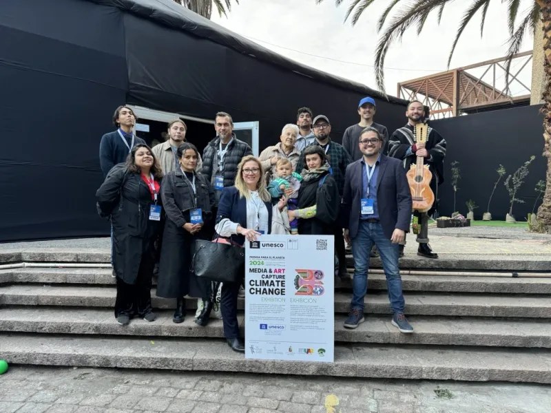 The artists, accompanied by Ma’aly Hazzaz, Coordinator of UNESCO’s Multi Donor Programme on Freedom of Expression and Safety of Journalists (in front with glasses), pose with the artist statement board during the exhibition.. Photo by UNESCO.