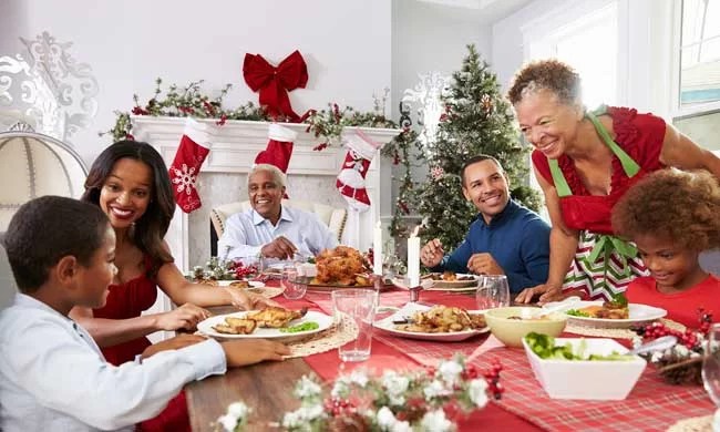 Family gathered around holiday table with foood and decorations.