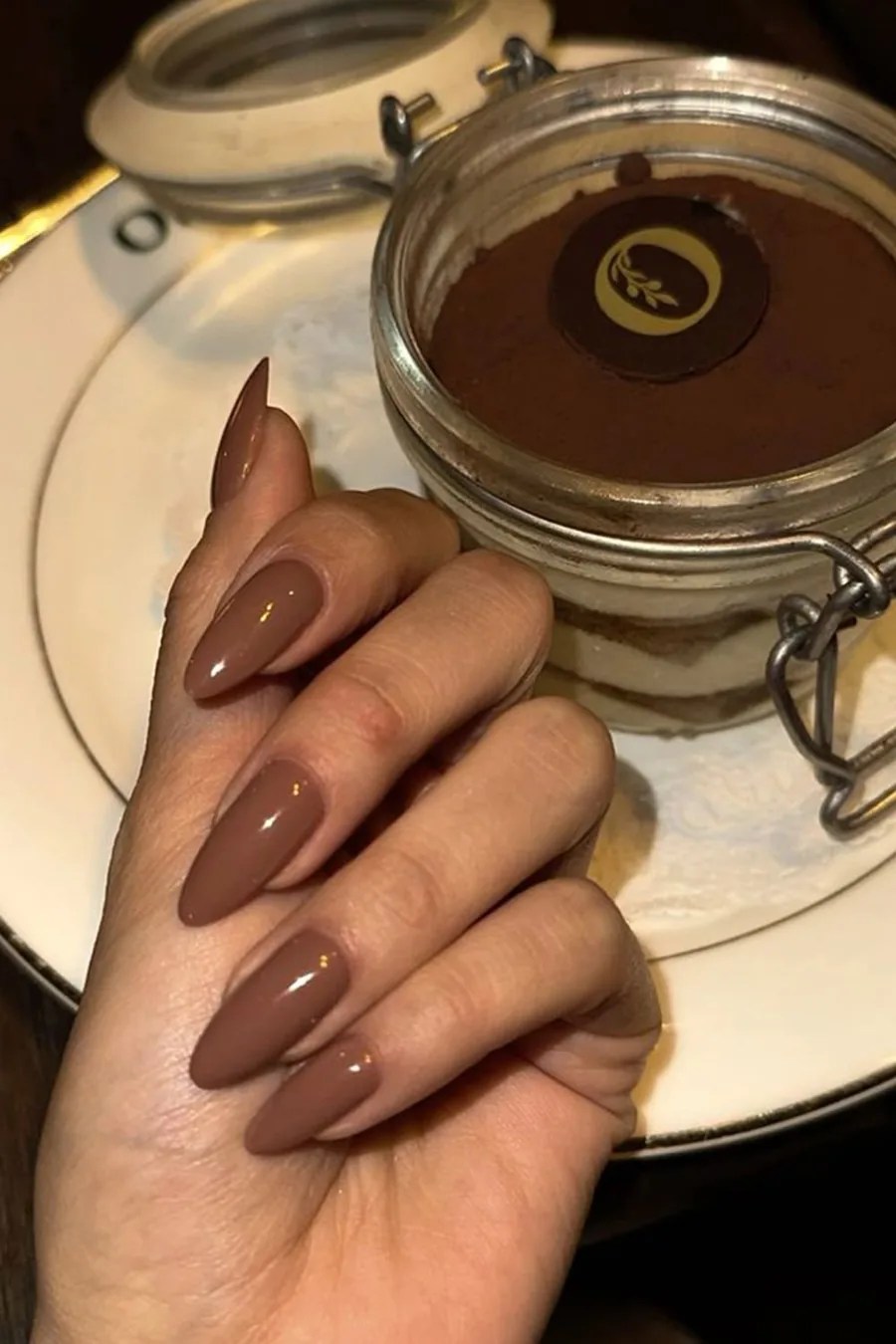 Glossy mocha brown almond nails beside a coffee dessert for a warm fall manicure
