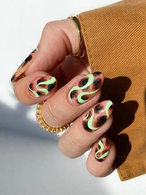 Close-up of trendy summer 2025 nail design featuring lime green swirls, black glitter accents, and subtle leopard print on short natural nails.