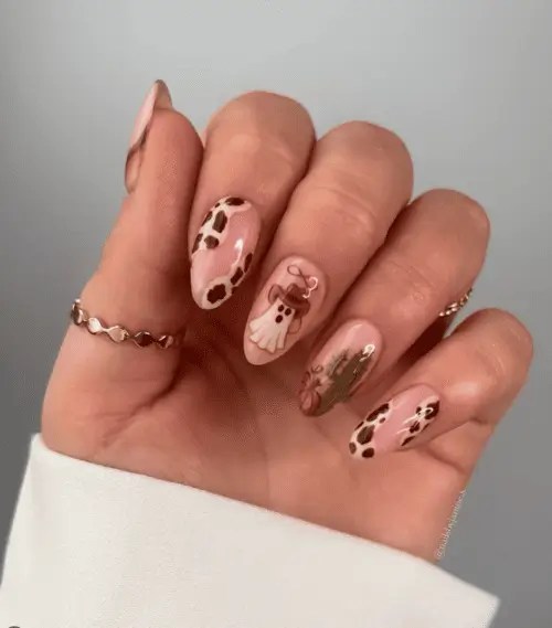 Spooky Western nails featuring cowboy ghost, cow print irregular nails, and cactus and pumpkins accent nail is neutral and adorable for Halloween