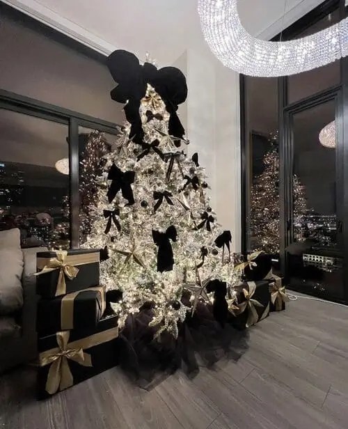 Black and white Christmas tree decorated with oversized black bows, white lights, and matching black-and-gold wrapped gifts.