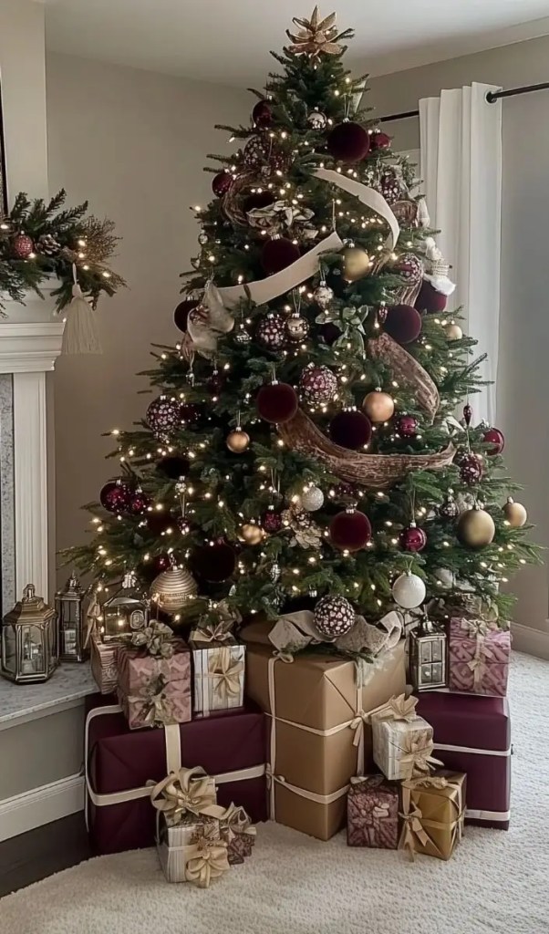 Burgundy and gold Christmas tree decorated with velvet ornaments, metallic baubles, ribbon, and glowing lights surrounded by matching presents.