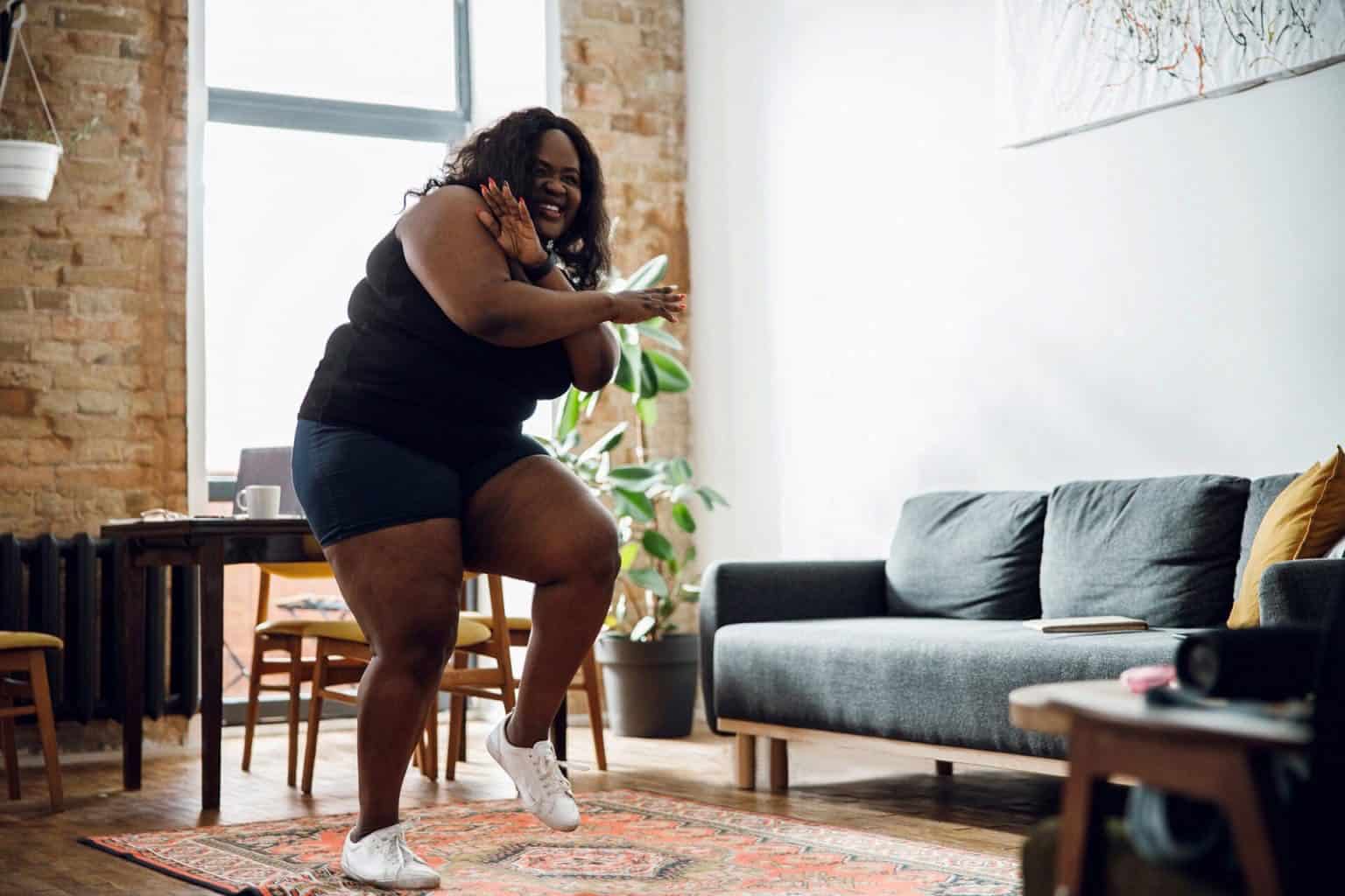A plus size Black woman dancing joyfully in her living room as a form of fun and effective home exercise