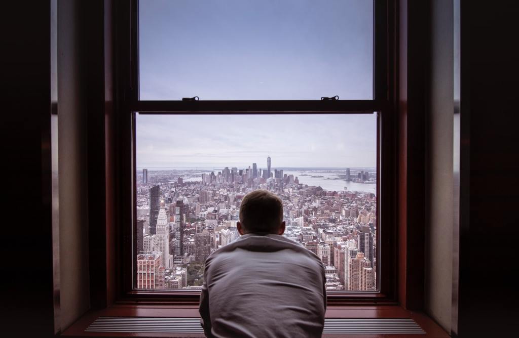 view from behind man looking out window on to metropolis below, get started setting goals