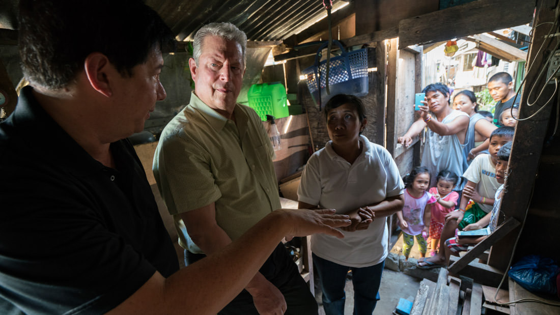Two men interacting in a rustic indoor setting with several onlookers.