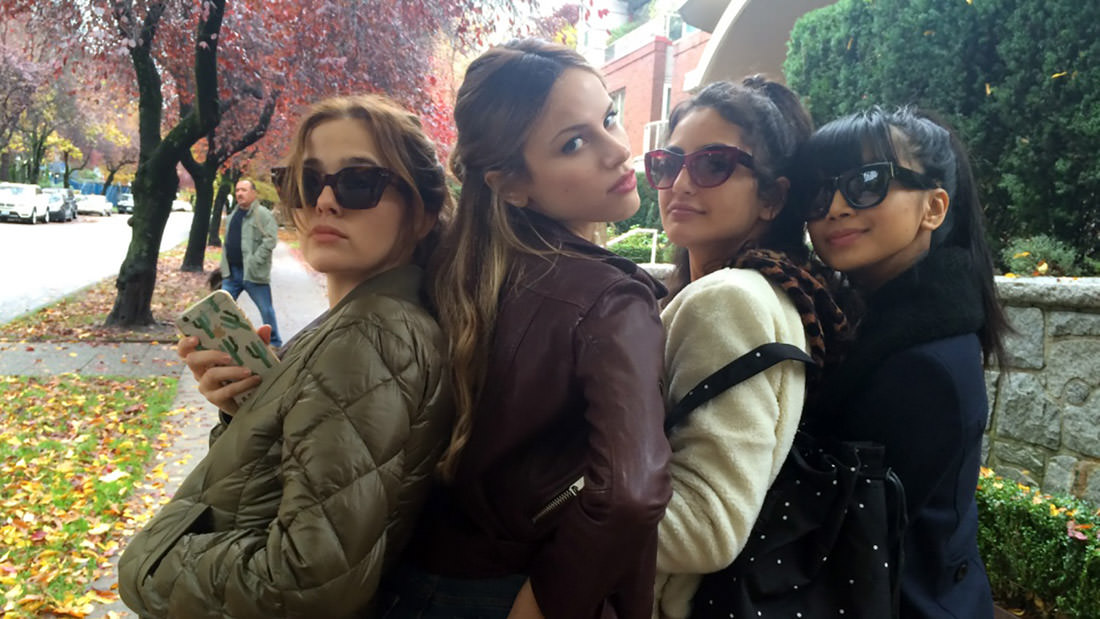 Four women posing together at an outdoor event, wearing sunglasses and jackets.