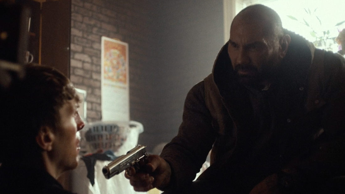 A tense moment as a man points a gun at another seated man.