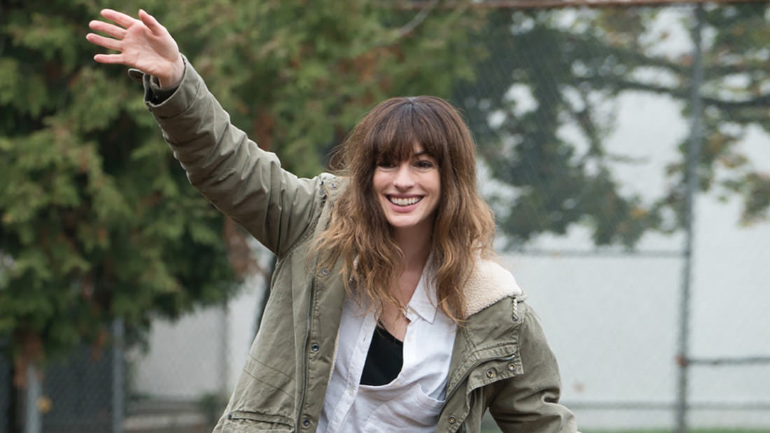 Smiling woman in a casual jacket waves outdoors.