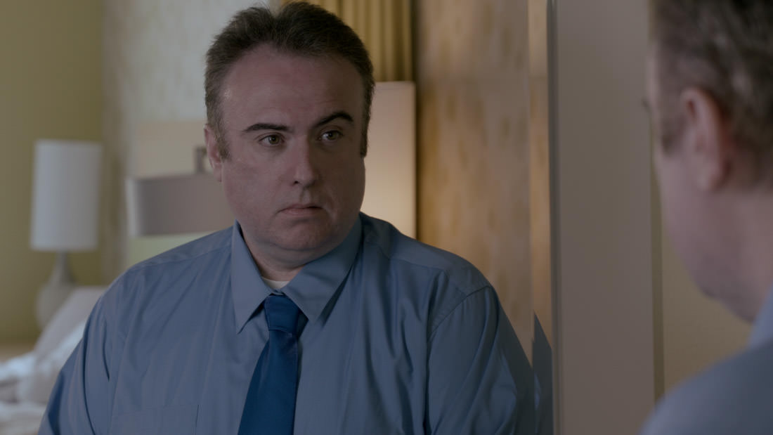 Man in a blue shirt and tie looking sideways indoors.