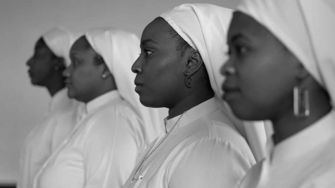Three women dressed in white, wearing head coverings, in a side profile.