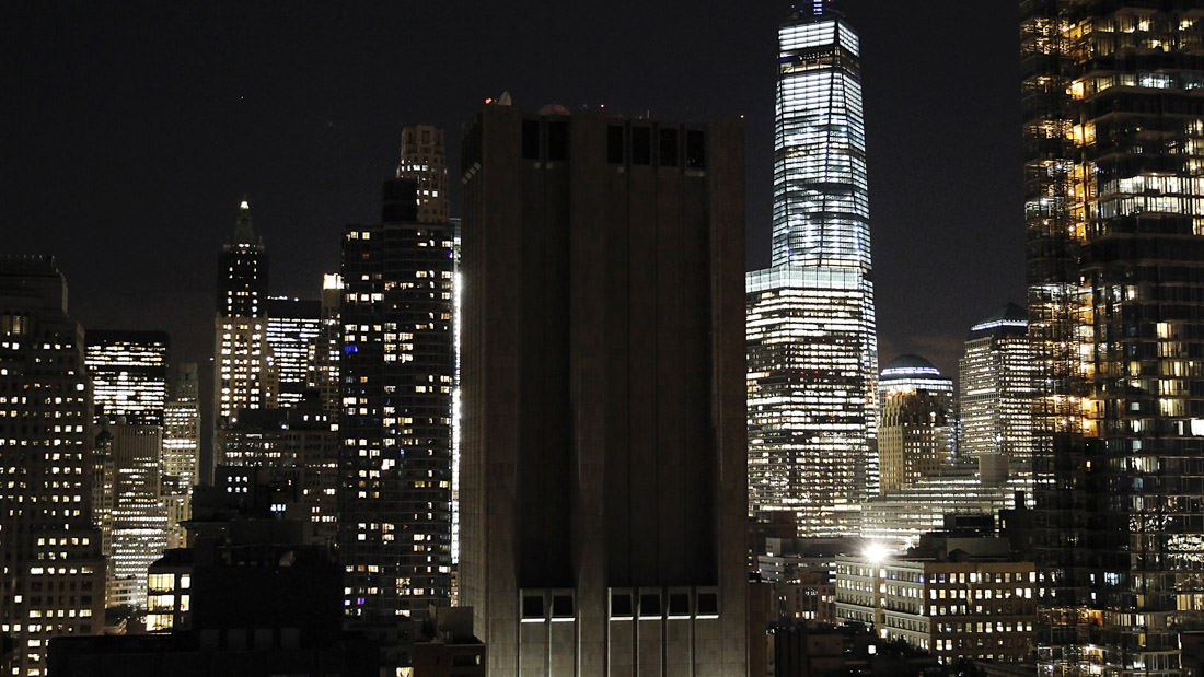 Nighttime cityscape featuring illuminated skyscrapers against a dark sky.