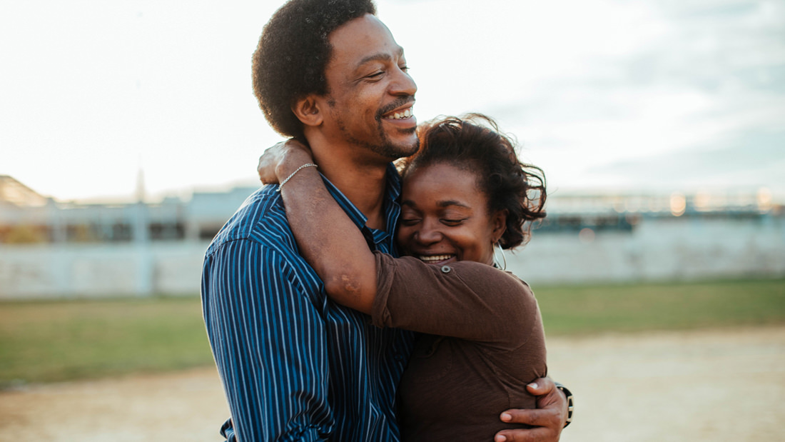 Couple warmly embracing outdoors with joyful smiles.