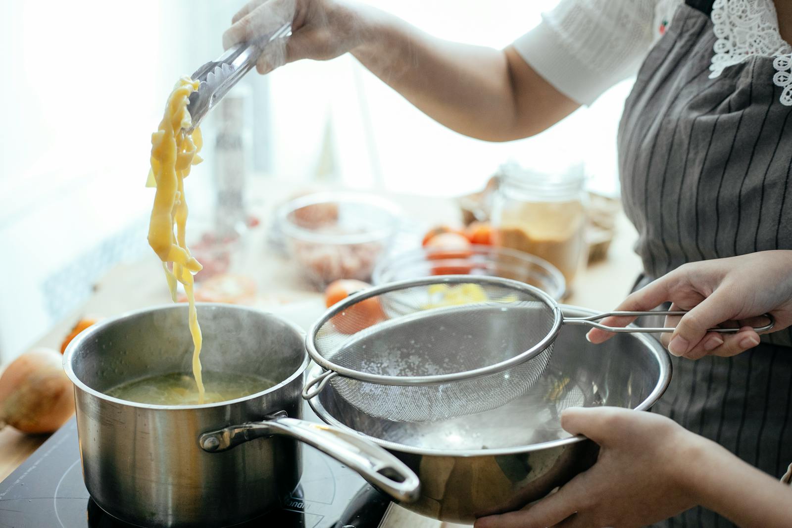 Tirokafteri Recipe- Delicious Greek Spread In 10 Minutes 7 Unrecognizable cooks with strainer putting pasta out of pan with boiling water while standing near stove in kitchen on blurred background