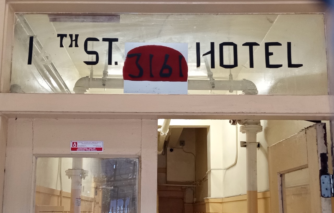 The front door of a hotel with the words 16th St. Hotel on the window, made out of tape, with the '6' missing.