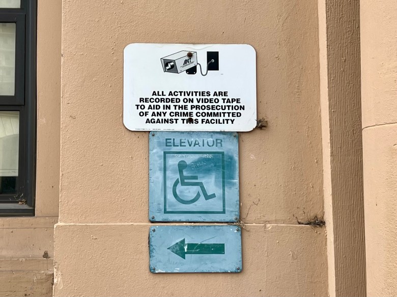 Signs informing people of security cameras and accessible elevator on outside of building