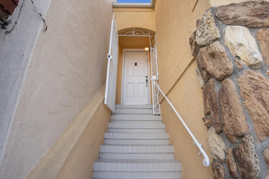 Stairs leading to a white front door with a decorative gate, surrounded by beige walls and a stone accent.