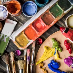 Assorted watercolor paints, brushes, and a wooden palette with bright paints ready for painting.