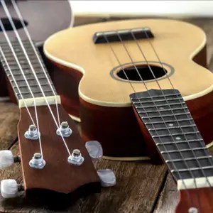 Two acoustic guitars on a wooden surface, close-up of tuners, strings, and fretboards.