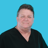 Smiling middle-aged man in black scrubs against a bright cyan background. The image is a simple portrait for professional context.