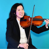 Woman in a black blazer playing a violin against a bright blue background, smiling at the camera.
