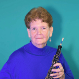 Portrait of an older woman in a purple sweater, holding a clarinet against a teal background.