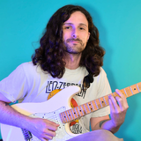 Musician with long wavy hair in a lavender shirt playing a red electric guitar against a teal background.