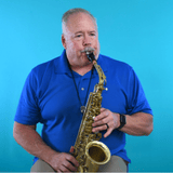 Older man in a blue polo shirt playing a saxophone against a bright blue background, seen from the waist up.