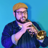 Man wearing a mustard cap and glasses, playing a trumpet against a bright blue background.