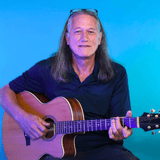 Man with long hair in a dark shirt playing an acoustic guitar against a blue gradient background, looking toward the camera.