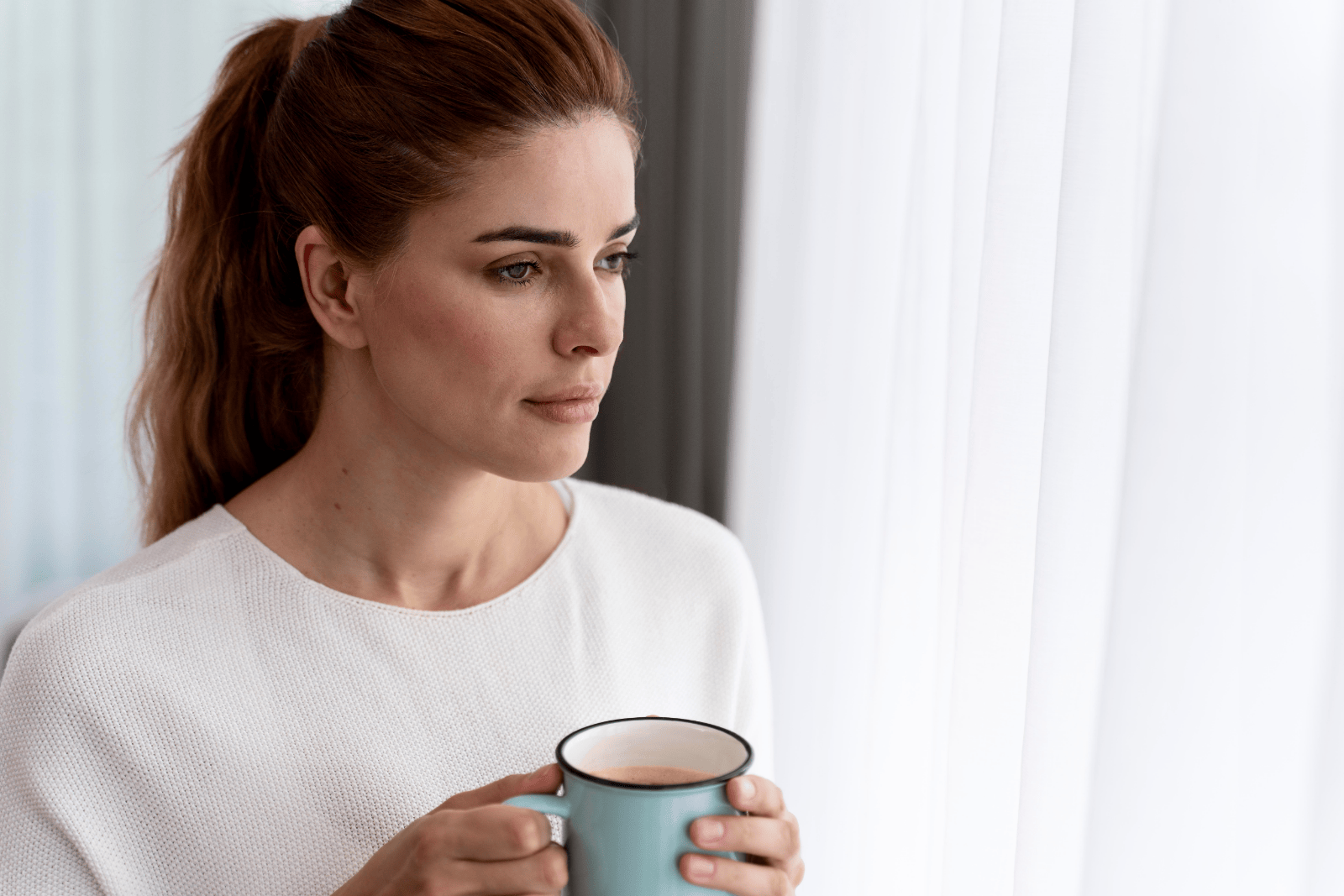 Woman standing with coffee looking out a window in a quiet morning moment