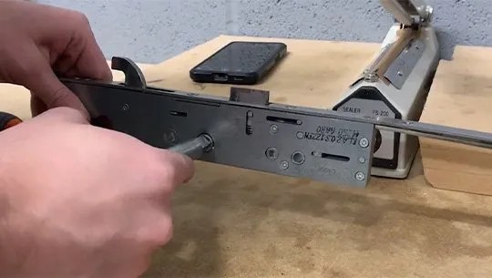 A person testing a door lock mechanism with a screwdriver on a workbench