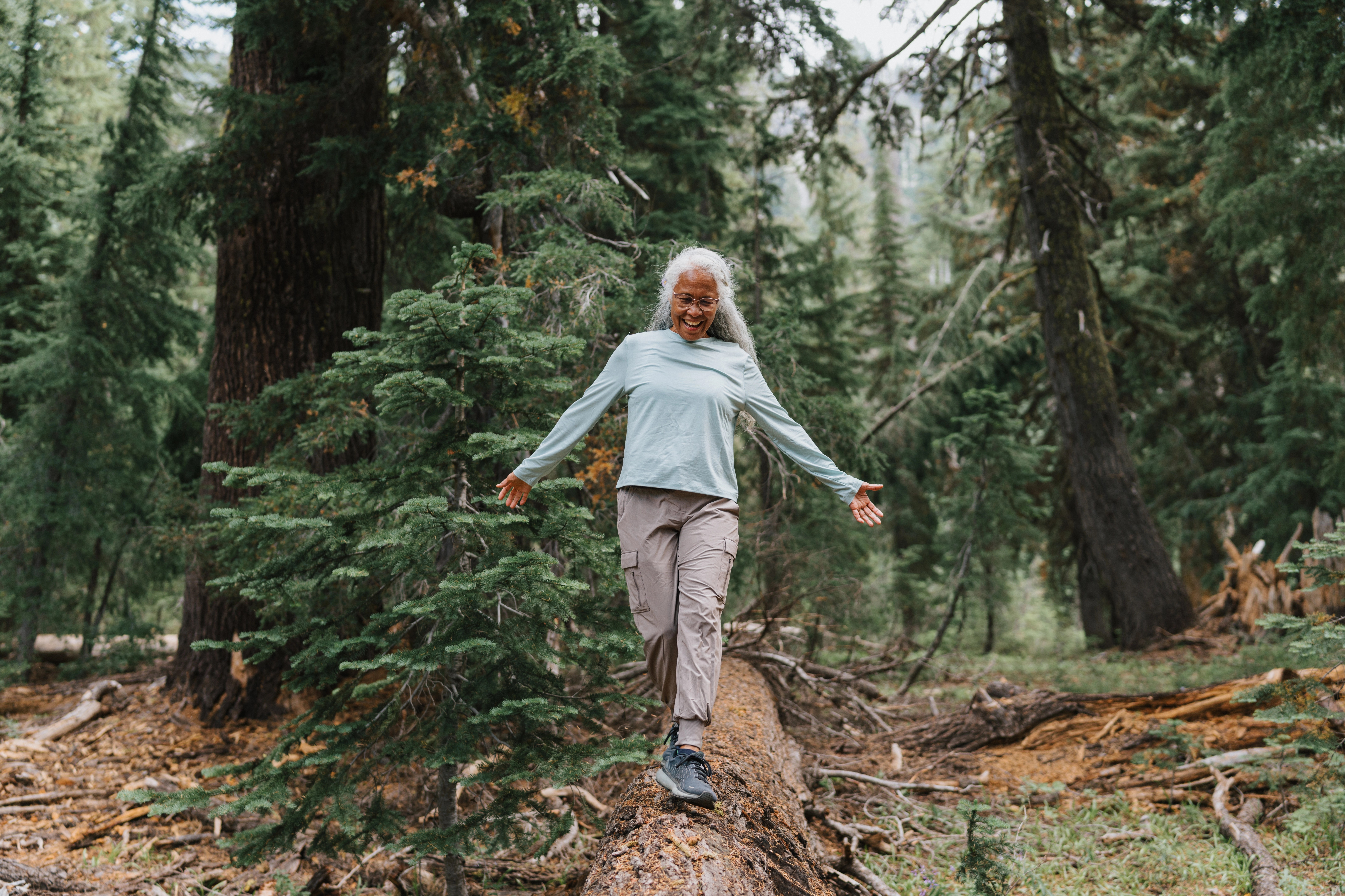 Older woman balancing on a fallen log while hiking in a forest