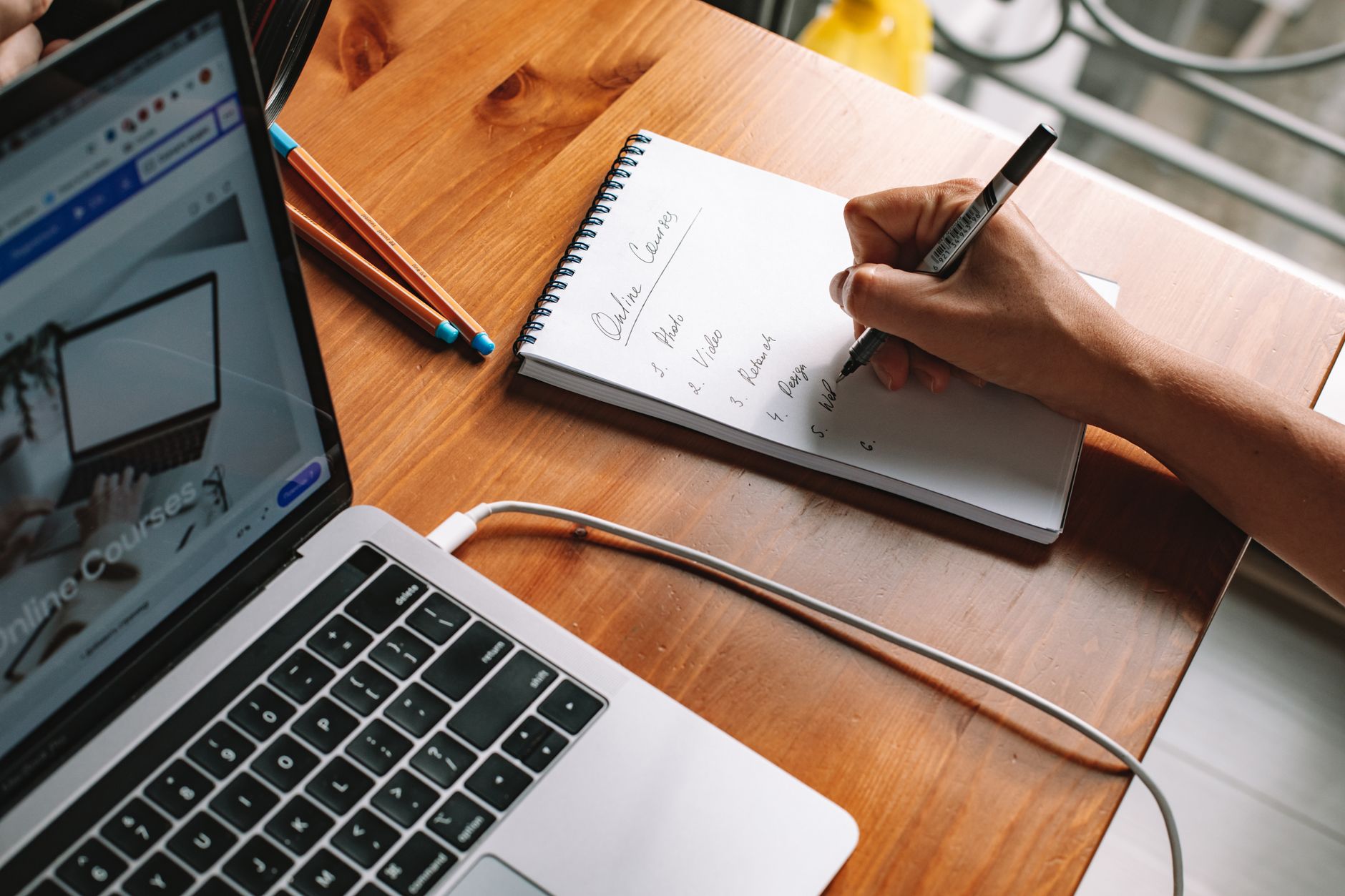 person writing on a notepad beside a laptop