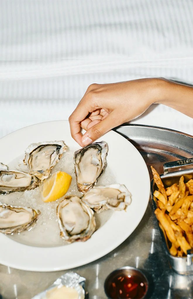 Photo of a model hand eating oysters and fries in her hotel room.