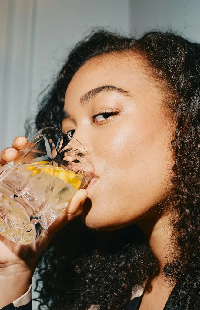 Photo of a model drinking a cocktail beverage out of a clear glass.