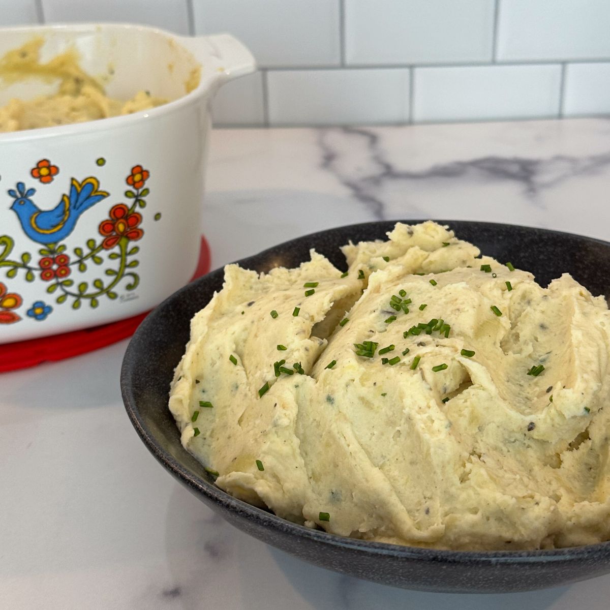 Bowl of whipped potatoes in front of. baking dish of whipped potatoes.